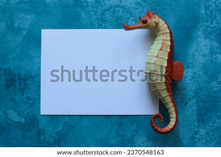 blank paper card with a toy seahorse on a blue watercolor background