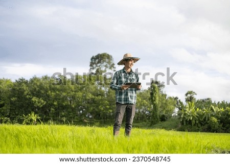 A male farmer uses a tablet to collect data from his rice fields to sell in the online market. Modern Farmer Royalty-Free Stock Photo #2370548745