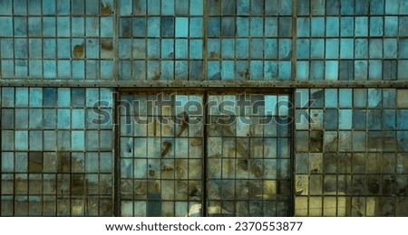 Broken windows on an old abandoned industrial factory building, framed by rusty metal and smudged by dirty glass. A widescreen image with the blue sky reflecting in the panes. Royalty-Free Stock Photo #2370553877