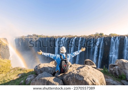 Man sitting on the top of a rock enjoying the Victoria Falls - Zimbabwe Royalty-Free Stock Photo #2370557389
