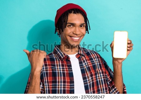 Photo of optimistic guy cornrows checkered shirt hold smartphone indicating at eshop empty space isolated on teal color background