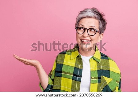 Portrait of cheerful person with gray hairdo dressed plaid shirt arm presenting object look empty space isolated on pink color background