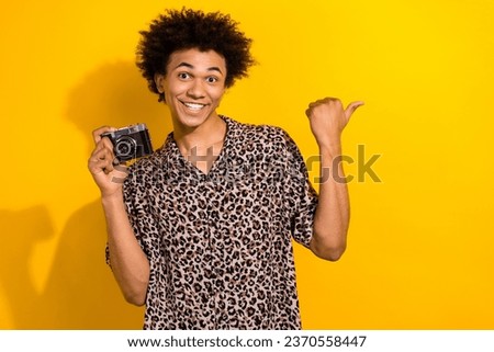 Photo of positive nice guy with afro hairdo dressed leopard shirt hold camera directing empty space isolated on yellow color background