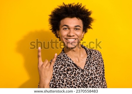 Portrait of toothy beaning cheerful person with chevelure wear leopard shirt showing rock symbol isolated on yellow color background