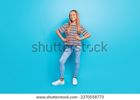 Full size photo of adorable cool teen girl wear colorful t-shirt denim pants hold hands on waist isolated on blue color background