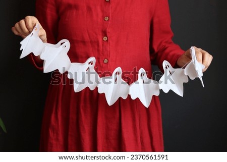 Halloween preparations. Young woman holding festive garland on black background with copy space.  Halloween decorations close up photo. 