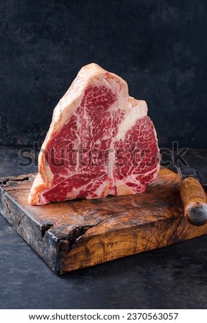 Raw dry aged wagyu porterhouse beef steak offered as close-up on rustic old wooden board with a knife  Royalty-Free Stock Photo #2370563057