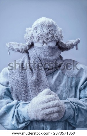 A frozen man with his hands clasped all bundled up in a fur trappers hat, scarf, parka and knit gloves, covered in snow and frost.