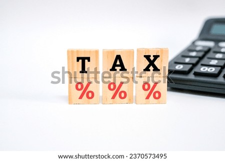 A wooden block with icon percentage symbol and word tax beside calculator. Interest rate financial and mortgage rates concept