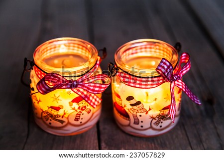 Christmas candle in a glass with drawings of snowmen and snow. Beautiful Burning festive candle tied with a ribbon on an old vintage background