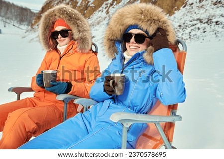 Winter holidays. Two beautiful girls in bright downy overalls enjoy their vacation at the ski resort. Alpine skiing, winter activities.