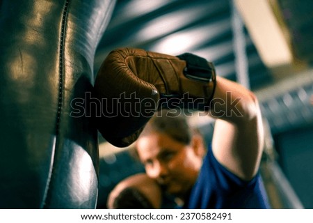 a girl boxer in gloves works out the strength of punches on a punching bag in the gym trains hard before fight close-up Royalty-Free Stock Photo #2370582491