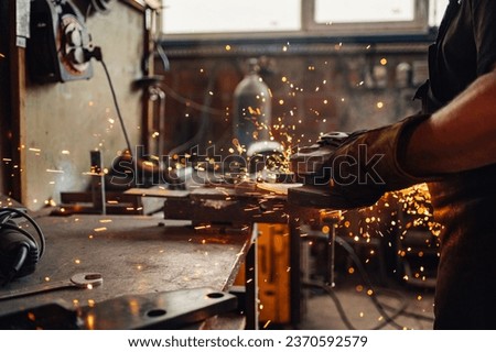 Man's hands in safety gloves holding a grinding machine in motion while golden sparks flying all around the working surface. Man working with an electric tool. Dangerous work concept. Copy space.