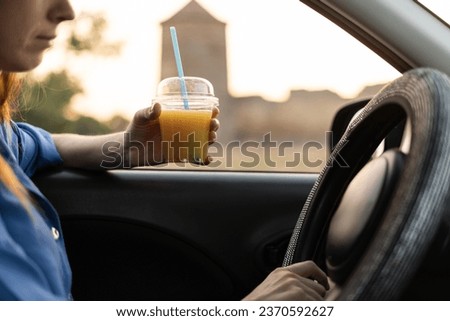 Young woman drinking her juice while sitting in a car while traveling through European cities, a fortress in the background. Copy space