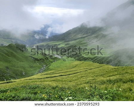 Cloudy Landscape with lush green alpine meadows of Himalayas in monsoon season. Clouds can be seen hovering over highlands. Shot during trek to Kalihani Pass near Manali in Himachal Pradesh,India Royalty-Free Stock Photo #2370595293
