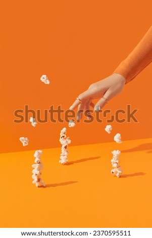Creative composition womans hand with popcorn on an orange background