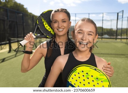 Two padel tennis players with rackets. Woman and girl teenager athlete with paddle racket on court outdoors. Sport concept. Download a high quality photo for the design of a sports app or web site.