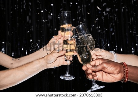 Closeup of hands toasting with champagne glasses at party against glittering background with confetti Royalty-Free Stock Photo #2370613303