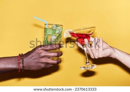 Close up of multiethnic young couple holding two cocktails against vibrant yellow background
