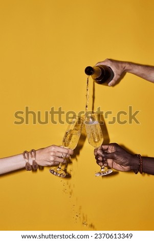 Pop color closeup of hands pouring champagne with splashes against vibrant yellow background Royalty-Free Stock Photo #2370613349