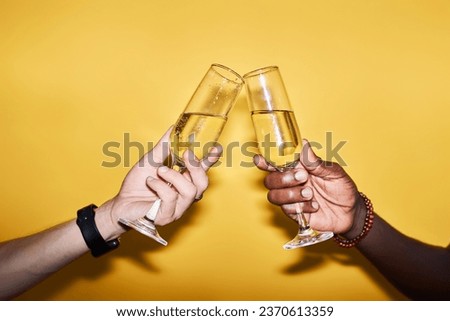 Close up of two people clinking champagne glasses against vibrant yellow background in celebration