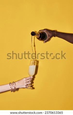 Vertical pop color concept of hands pouring champagne in glass on vibrant yellow background Royalty-Free Stock Photo #2370613365