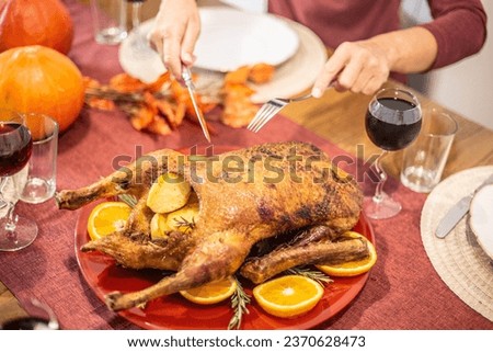 Photo top view Woman's hands holding a fork and a knife bring a chicken or duck to a turkey, ready to untie and enjoy the food. Bird stuffed with potatoes garnished with oranges and rosemary. 