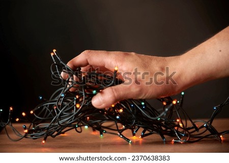 Christmas scene: young hand grabbing a decorative string of colored lights. Composition with copy space. Royalty-Free Stock Photo #2370638383