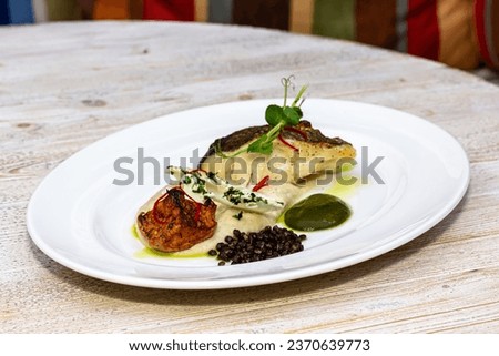 Fried Danish skrei cod fish filet with baby zucchini and lettuce as closeup on a modern design plate