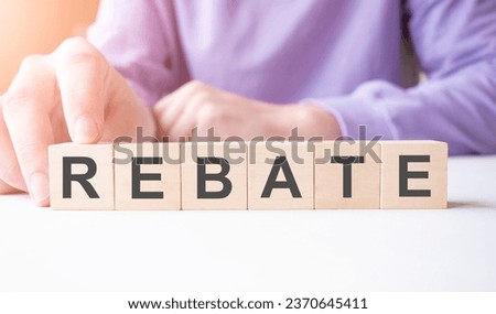 Businessman hand holding wooden cube block with REBATE business word on table background.