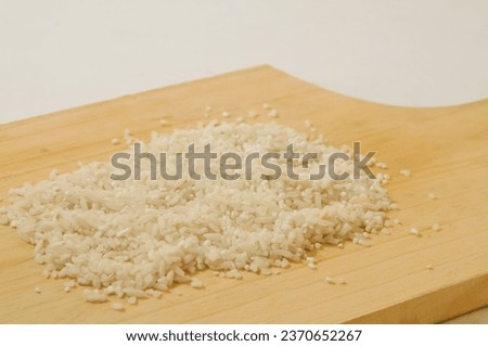 A pinch of white rice on a wooden cutting board isolated on a white background.