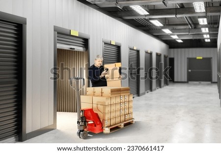 Man with boxes in warehouse building. Male rents storage unit. Guy near pallet jack. Businessman picks up goods from warehouse. Gate to storage unit is open. Man with phone leaves storage unit Royalty-Free Stock Photo #2370661417