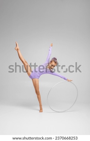 Rhythmic gymnastics. Gymnast child performs an exercise with hoop on white background in an purple swimsuit. Children's professional sports. Copy space