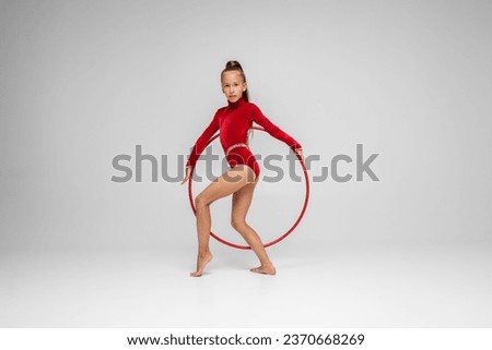 Rhythmic gymnastics. Gymnast child performs an exercise with hoop on white background in an red swimsuit. Children's professional sports. Copy space