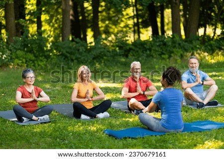 Group of senior people attending yoga class with instructor outdoors, older men and women sitting on mats in lotus position, practicing meditation, enjoying training outside, copy space Royalty-Free Stock Photo #2370679161