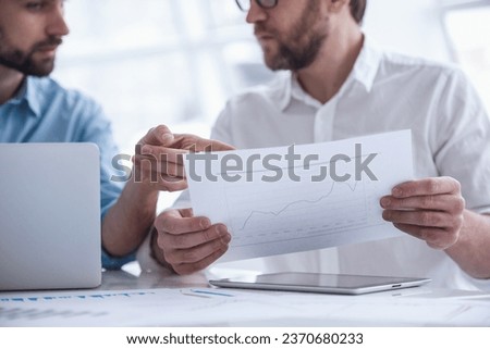 Two handsome businessmen are examining and discussing documents while working in office