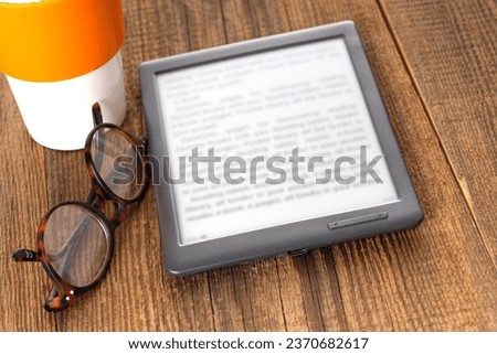 e-book reader and glasses on a wooden table.