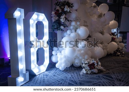An 18 decorative sign lit up, balloons and a sign form a backdrop at an 18th birthday party