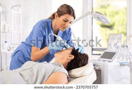 Skilled professional female aesthetician performing radiofrequency facial skin tightening procedure on mature woman in modern cosmetology clinic..Skilled professional female aesthetician performing Royalty-Free Stock Photo #2370705757