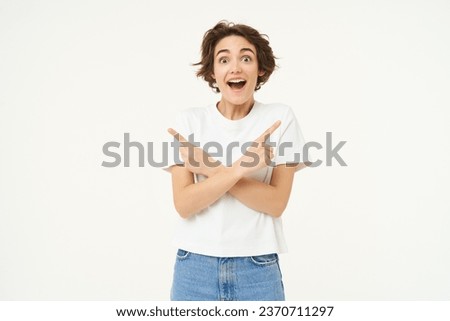 Portrait of amazed, happy young woman pointing sideways, left and right direction, showing advertisement, two choices, standing over white studio background.