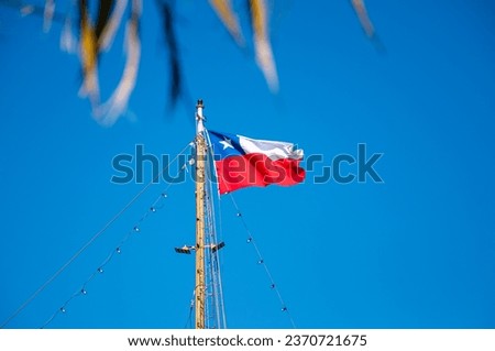 Flag of the Republic of Chile, on top of a  mast waving with blue sky as background.