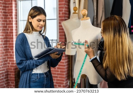 Portrait of young beautiful pretty owner business woman fashion designer stylish working.Attractive two young designer girl using tablet working with colorful fabrics at fashion studio