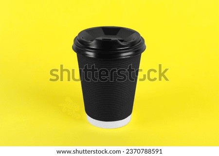 Black paper cup with plastic lid on yellow background. Coffee to go