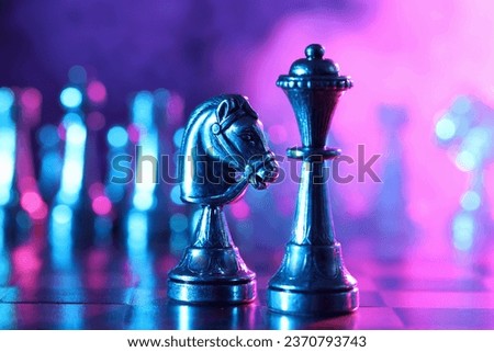 Queen and knight on chessboard in color light, selective focus
