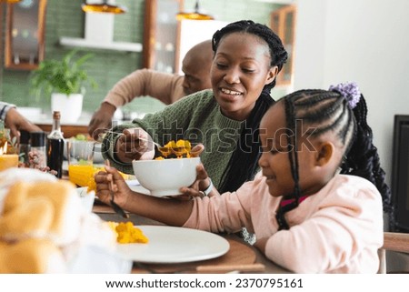 Happy african american mother serving food for daughter at thanksgiving dinner. Thanksgiving, celebration, meal, home, family, togetherness,