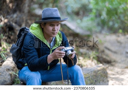 Hiking, Asian traveler taking beautiful photos Lifestyle and relaxation concepts Young Asian man with gray backpack takes beautiful blurred nature photo. and green forest areas