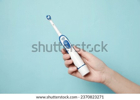 Woman holding electric toothbrush on light blue background, closeup