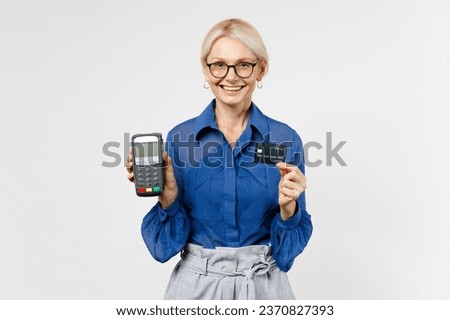 Blonde business woman 40s in blue classic shirt glasses formal clothes hold wireless modern bank payment terminal to process acquire credit card payments isolated on white background studio portrait.