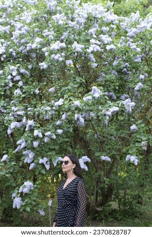 A beautiful girl of model appearance in a summer dress in a blooming garden among the aromas of bright lilac on a summer day.