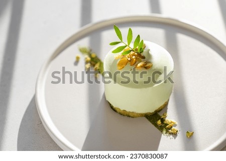 Vegan gluten free low calorie dessert. Round Pistachio mousse cake decorated with fresh pistachio greens, matcha on a light background with shadows. Trendy food styling. Restaurant, confectionery menu
